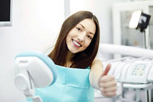 Woman in dental exam room giving the camera a thumbs up