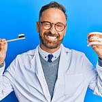 Dentist winking while holding up a toothbrush and dentures