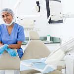 Portrait of female dentist in dental exam room standing near dental chair